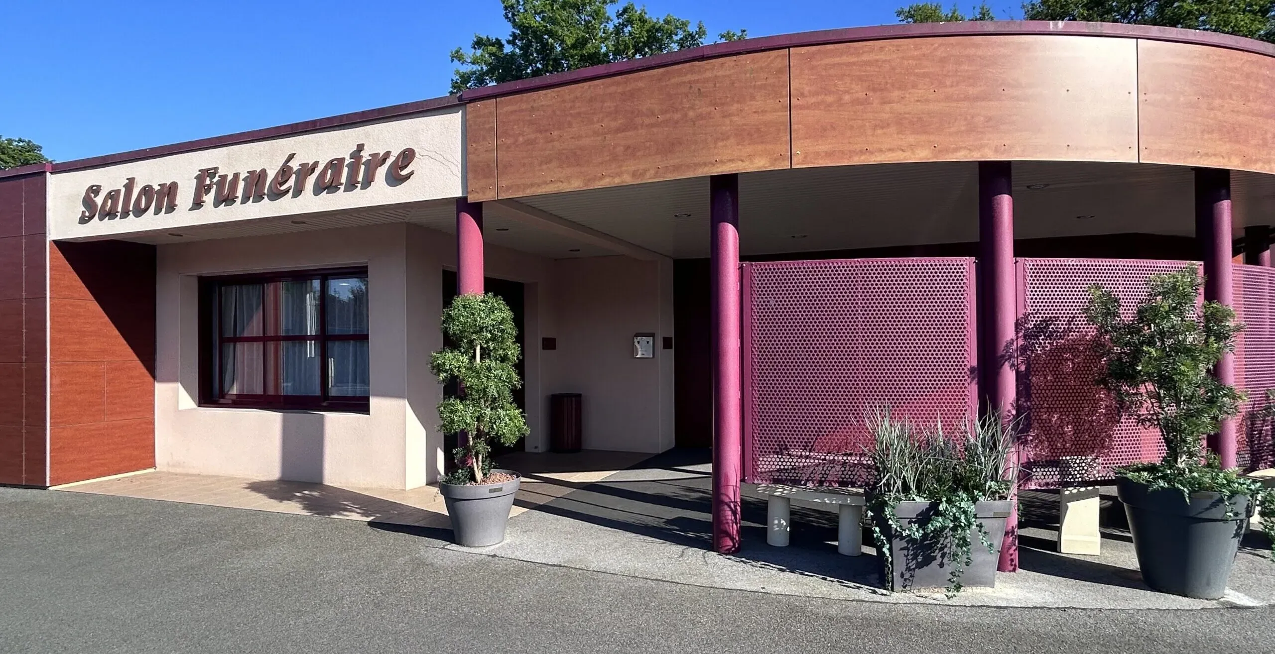 Entrée extérieure d'un salon funéraire moderne avec façade en bois et plantes en pot.